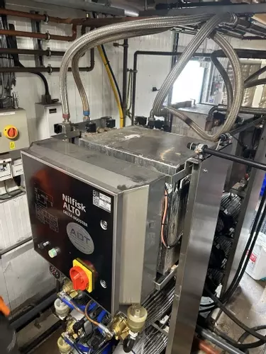 Original water tank installed on Nilfisk Delta Booster multi-pump pressure washer system before stainless steel tank replacement.